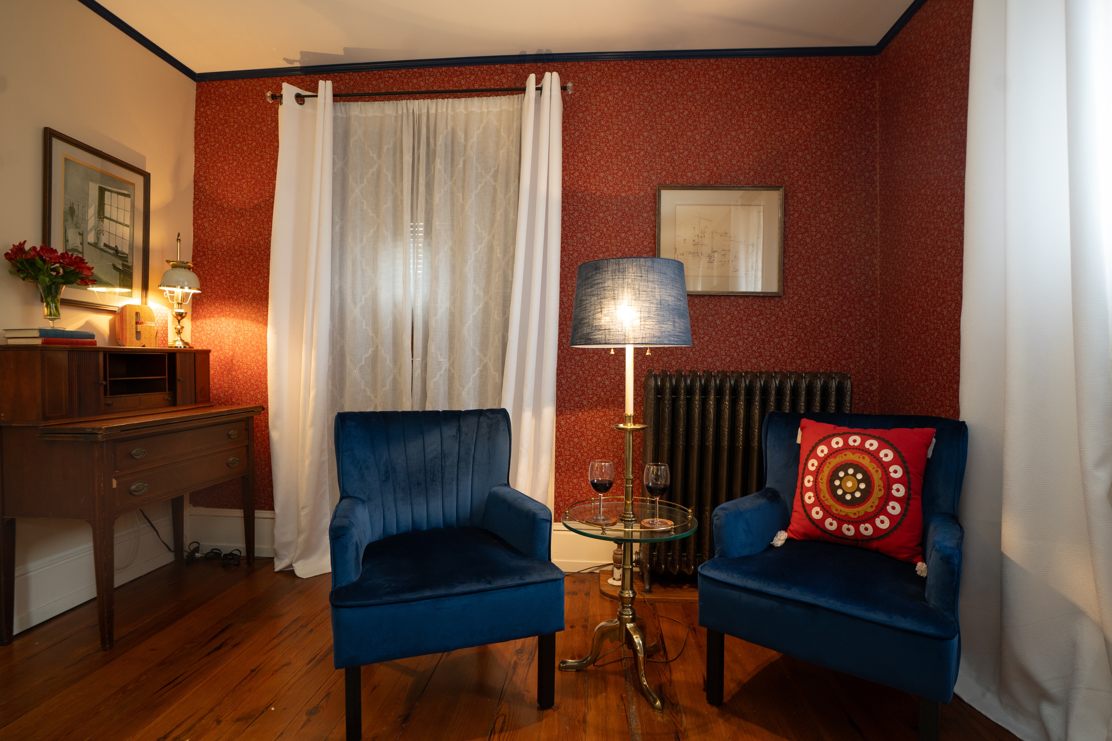 Two blue velvet scalloped armchairs sit on a hardwood floor next to a gold floor lamp with a patterned shade in a cozy seating area.