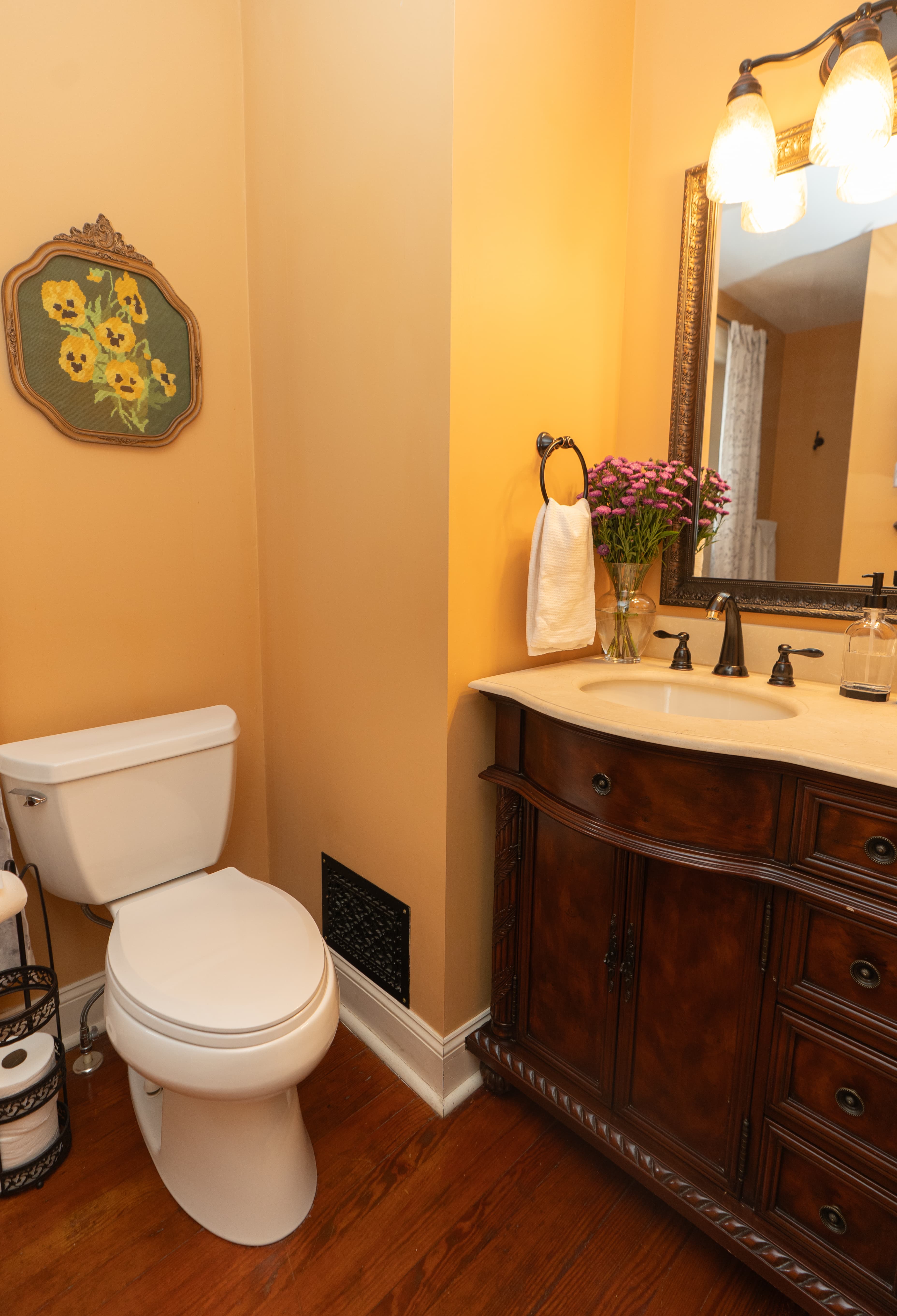 A single-sink bathroom vanity with a dark wood cabinet, white countertop, and oil-rubbed bronze faucet, set against warm peach-colored walls with a framed mirror.