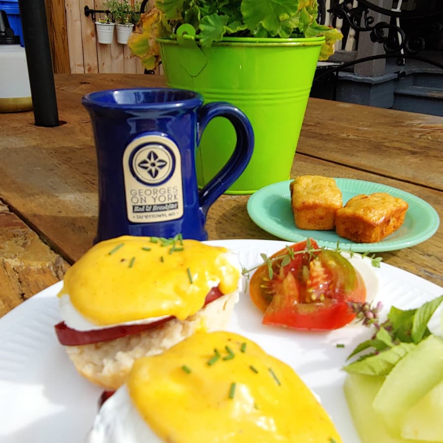 A plate of eggs Benedict with a side of salad, accompanied by a blue mug and a green plant on a wooden table.