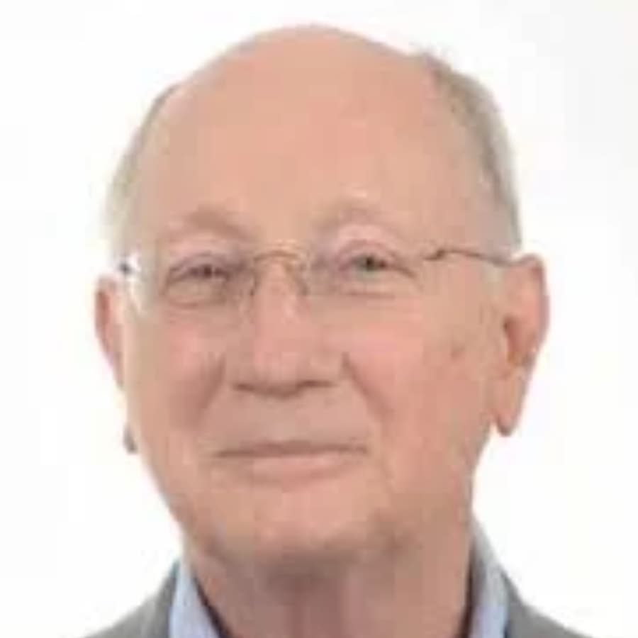 A senior man with glasses smiles against a plain background.