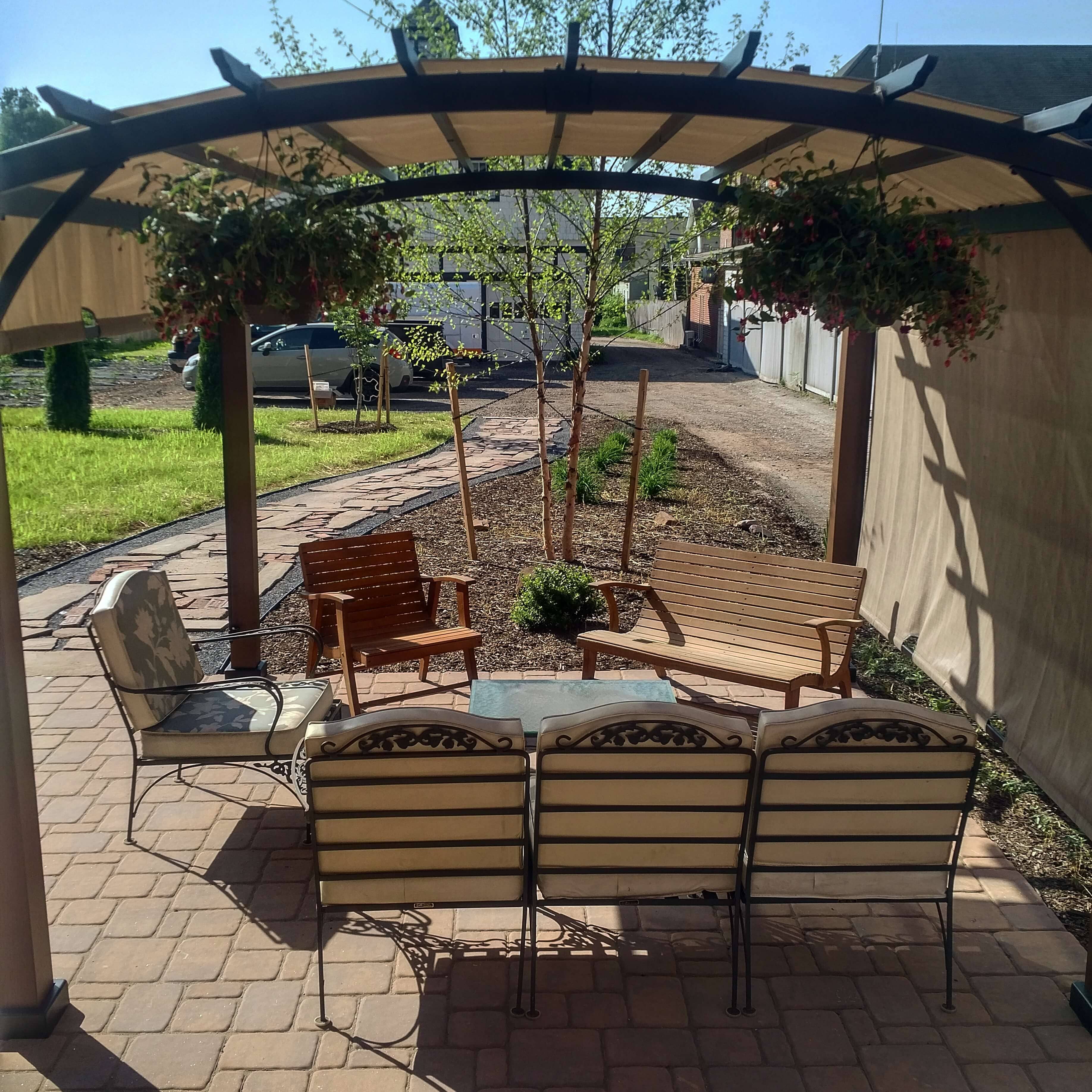 A cozy outdoor seating area beneath a pergola, surrounded by a green lawn and flowerbeds.