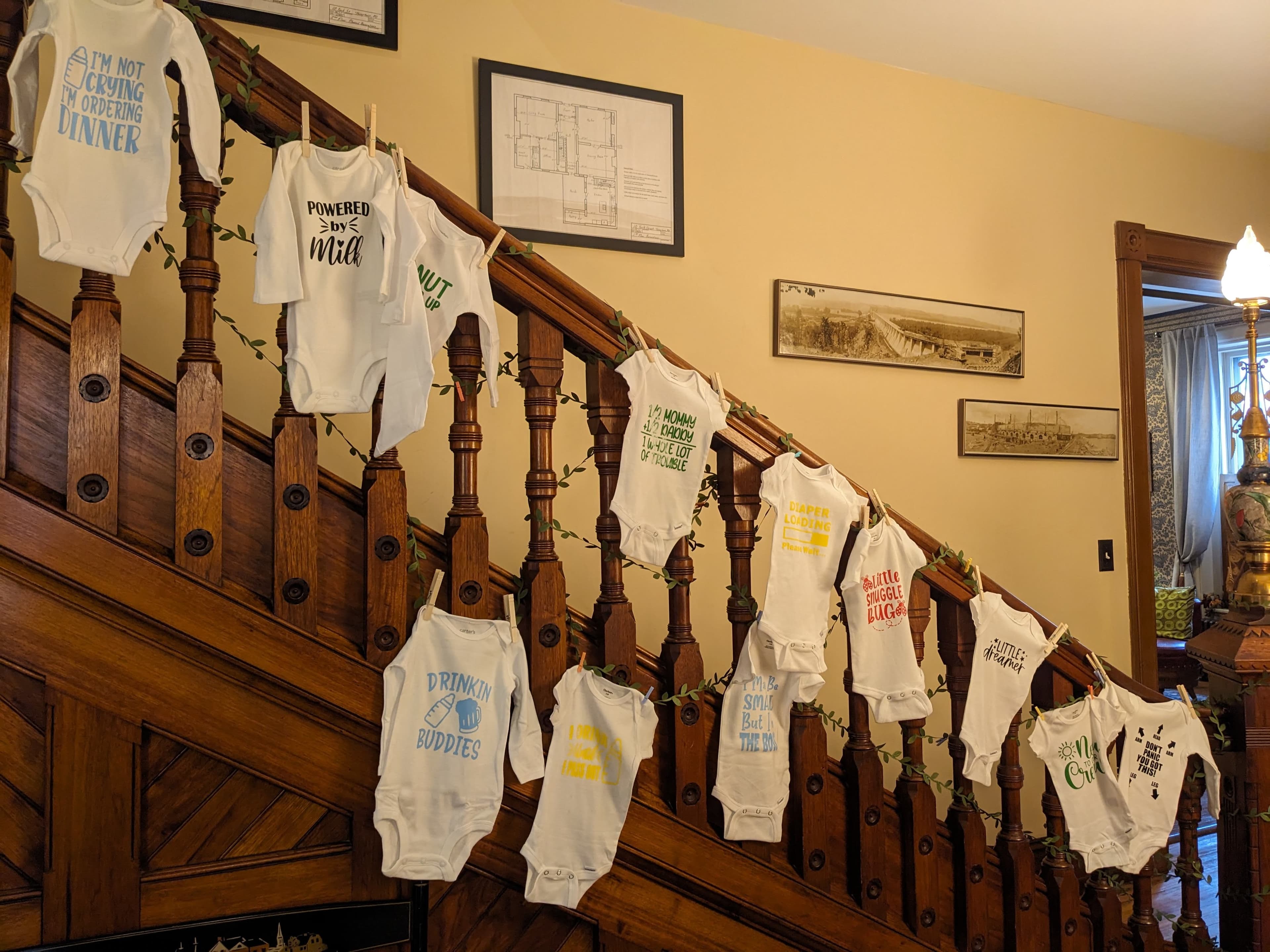 A staircase decorated with hanging baby onesies featuring playful phrases.