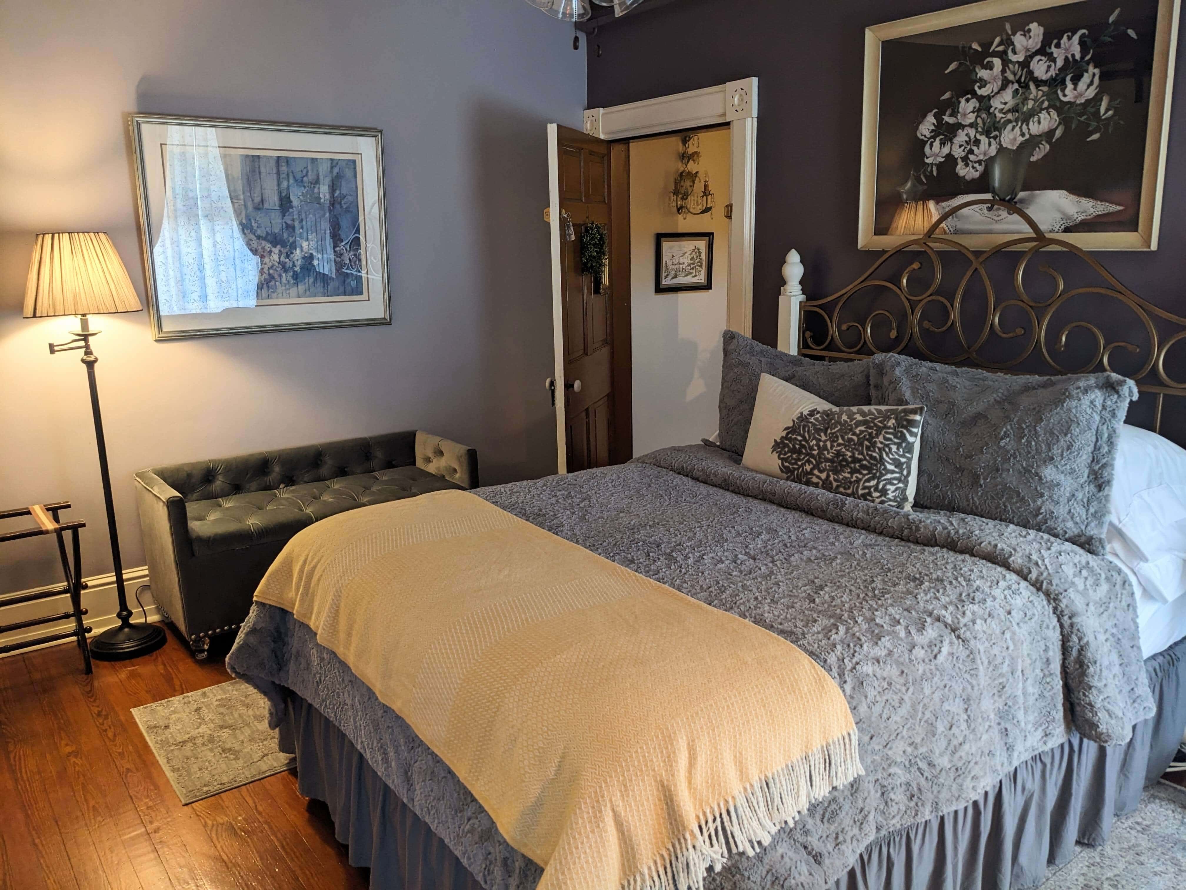 A cozy bedroom featuring a double bed with gray bedding, a decorative throw, a tufted bench, and soft lighting.