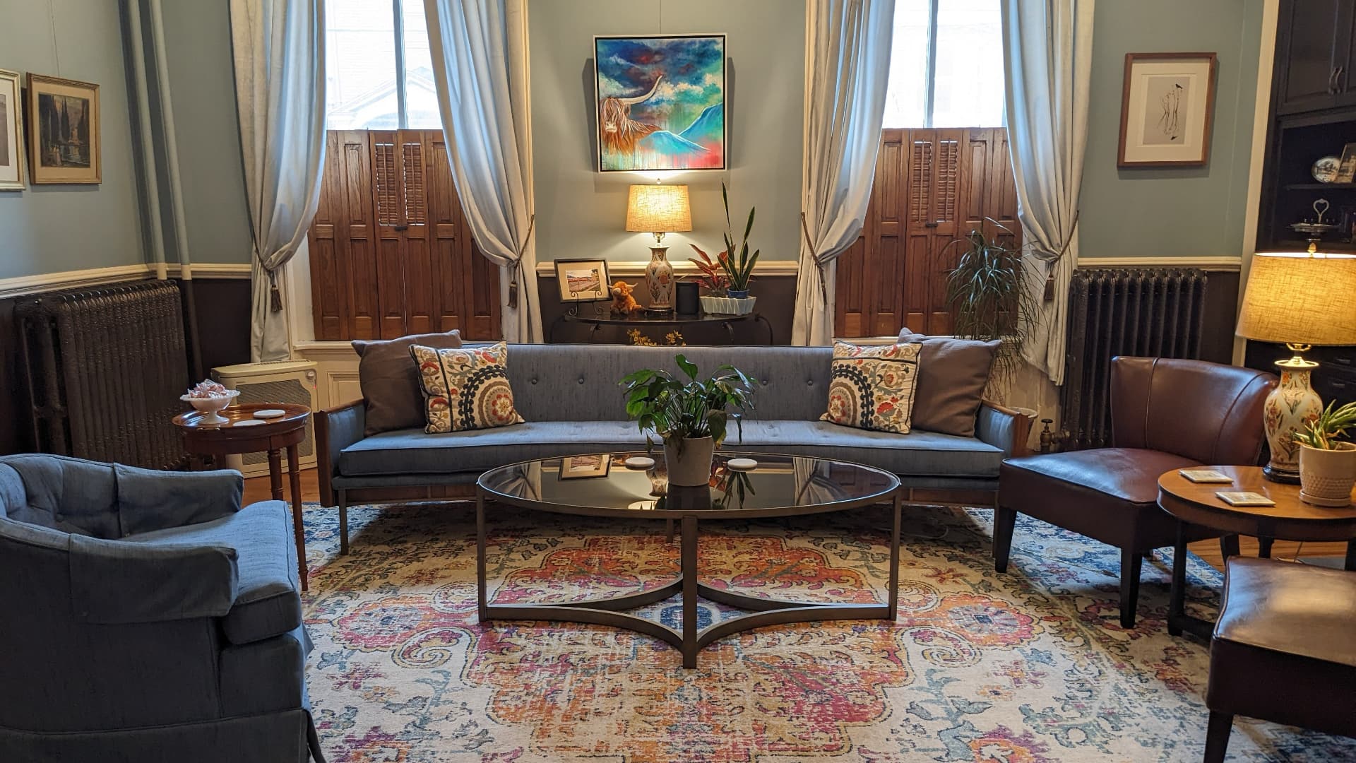 A cozy living room featuring a gray sofa, side chairs, and a coffee table on a colorful rug, with artwork and plants enhancing the decor.