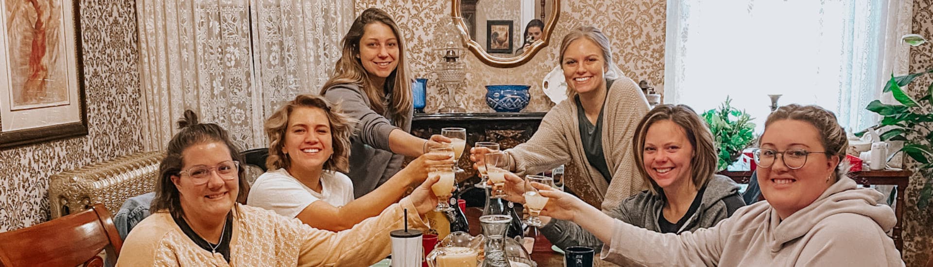 A group of six women celebrate with raised glasses around a dining table.