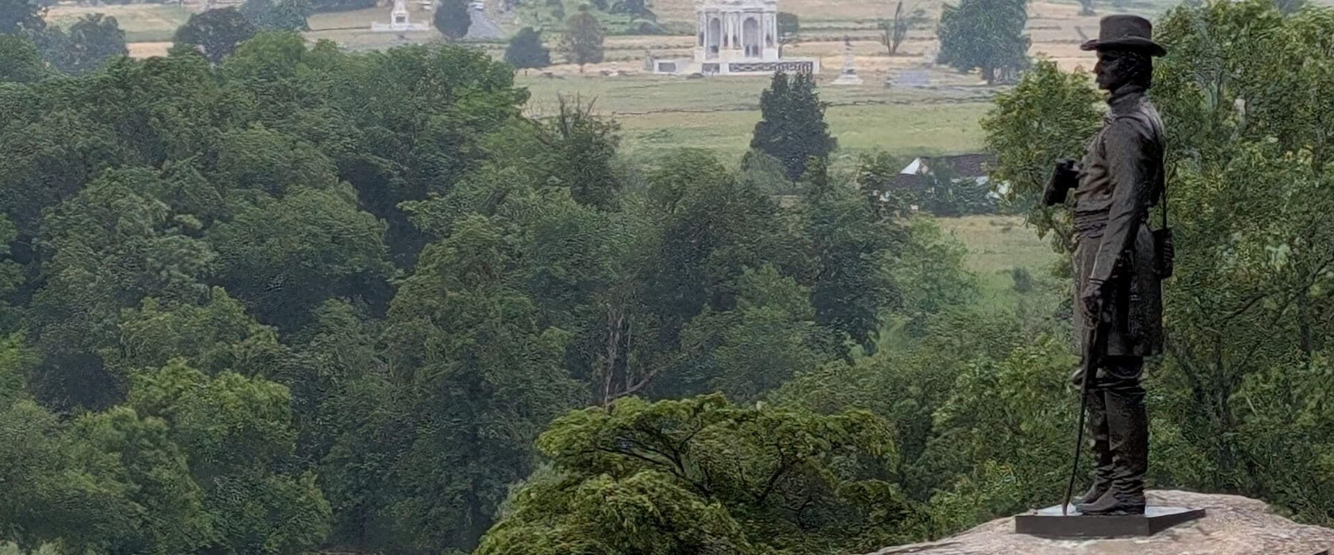 A bronze statue of a soldier stands overlooking a lush green landscape.
