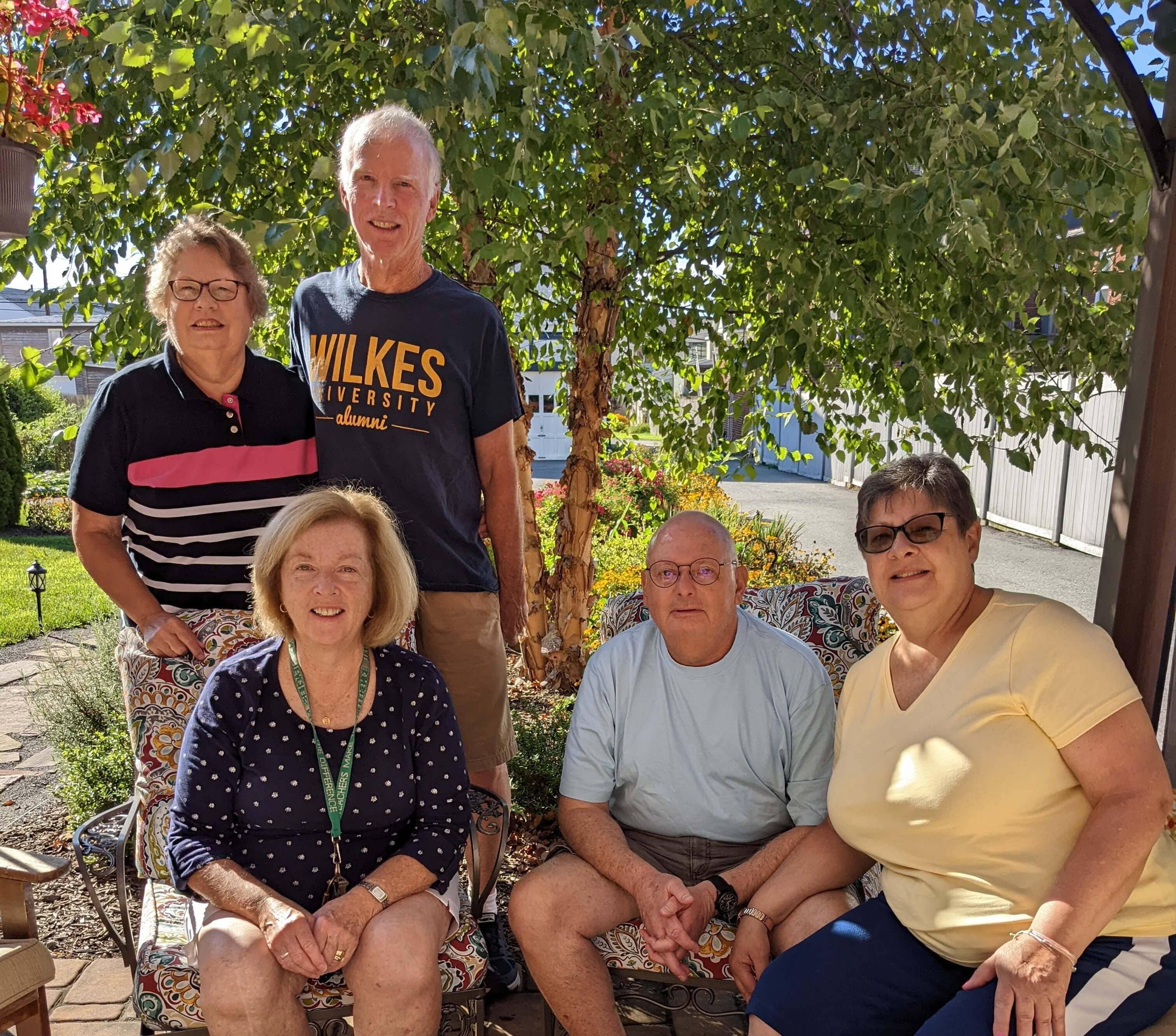 A group of five adults poses together outdoors in a garden setting.