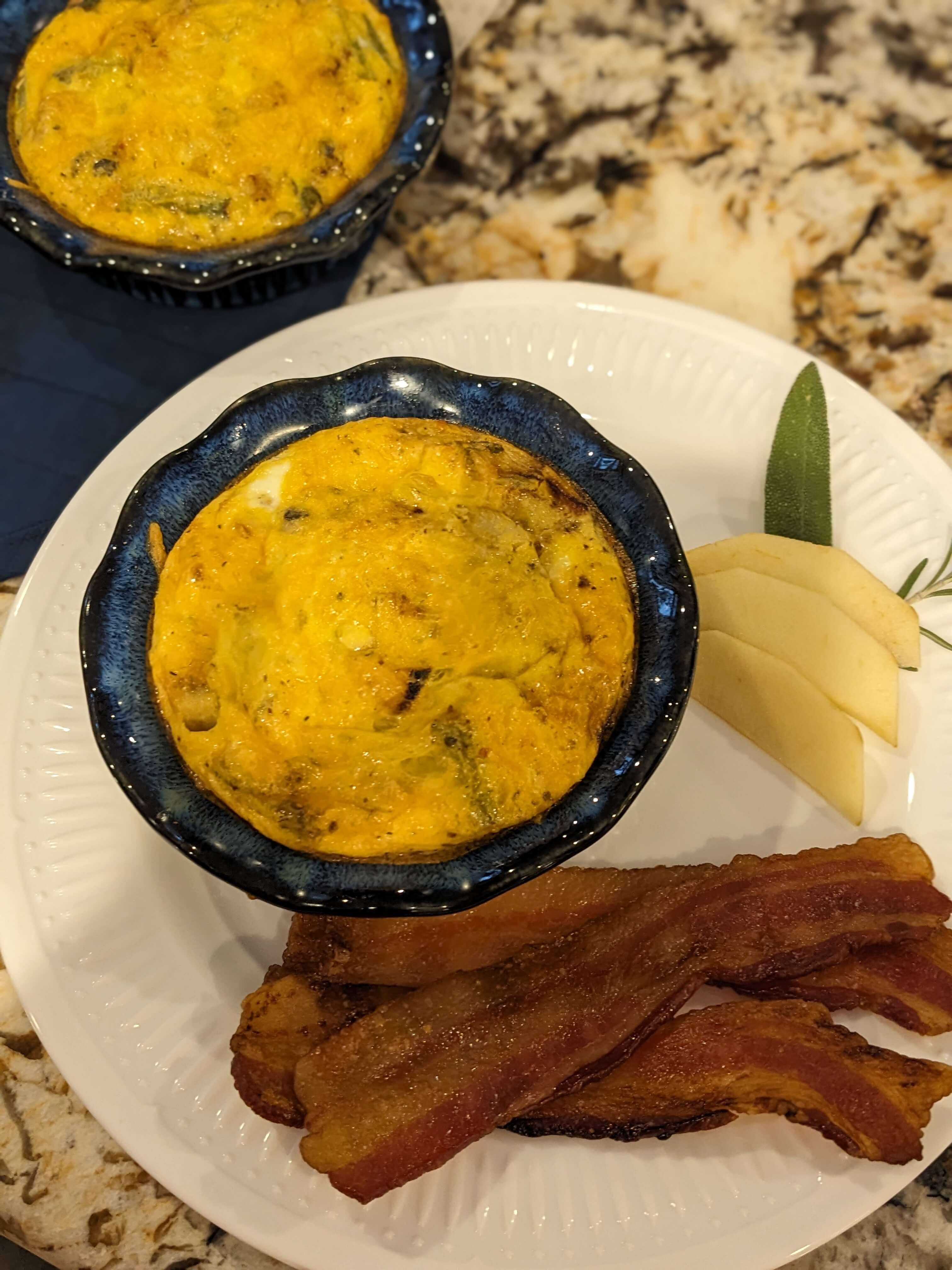 A plate with a baked egg dish, crispy bacon strips, and sliced apples.