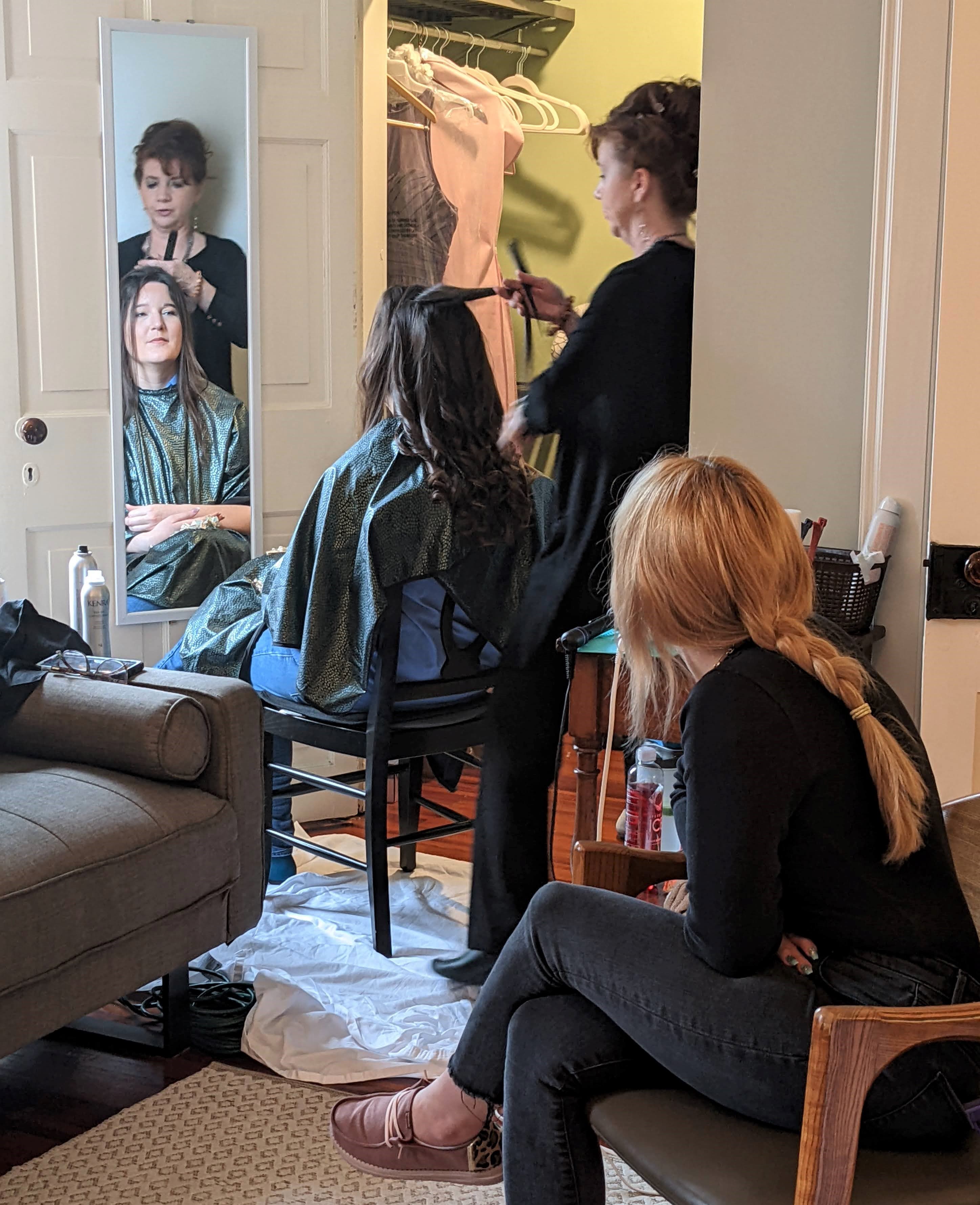 Two women are in a salon, one getting her hair styled while the other observes.