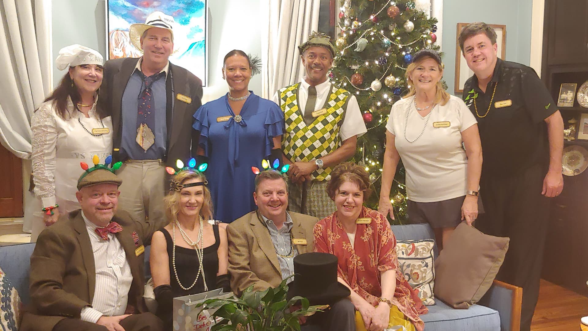 A festive group of people dressed in eclectic outfits poses together in front of a Christmas tree.