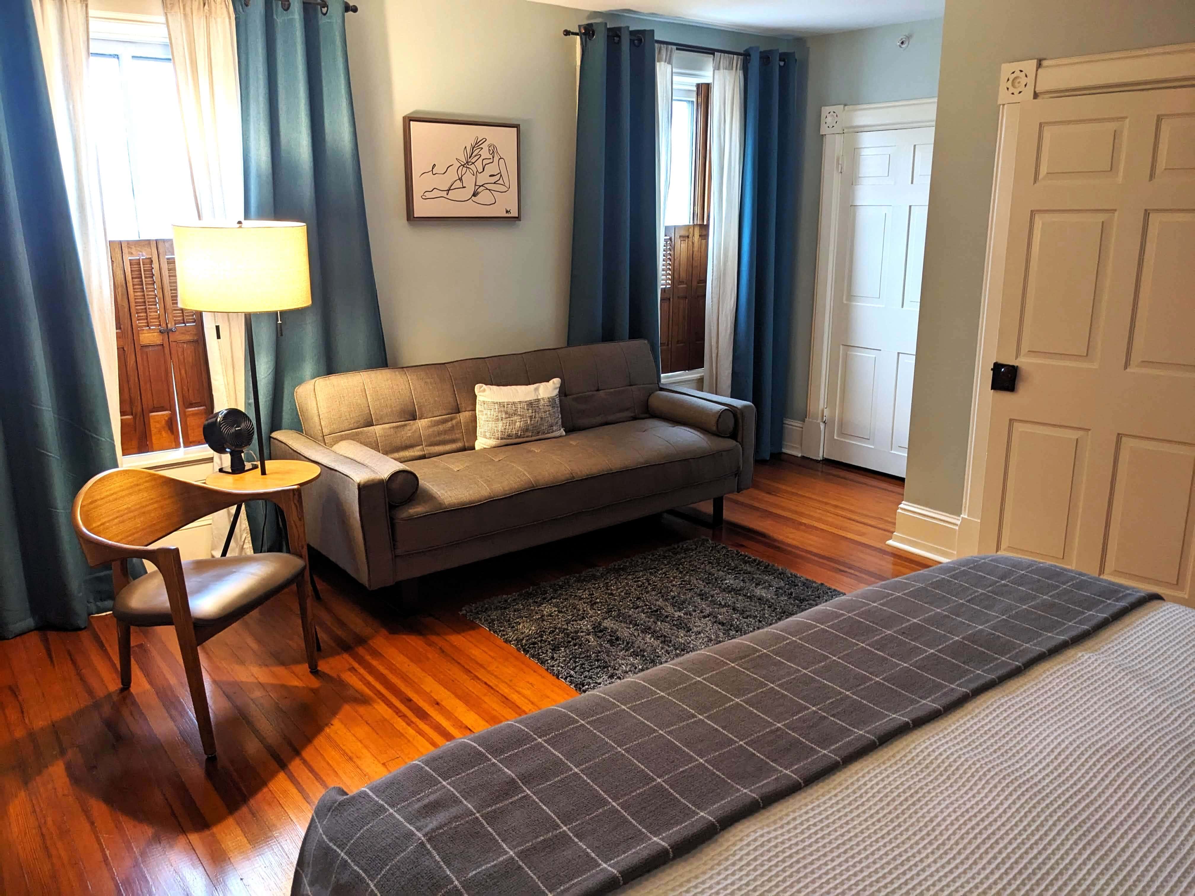 Cozy bedroom featuring a gray sofa, a lamp, a small table, and wooden flooring.