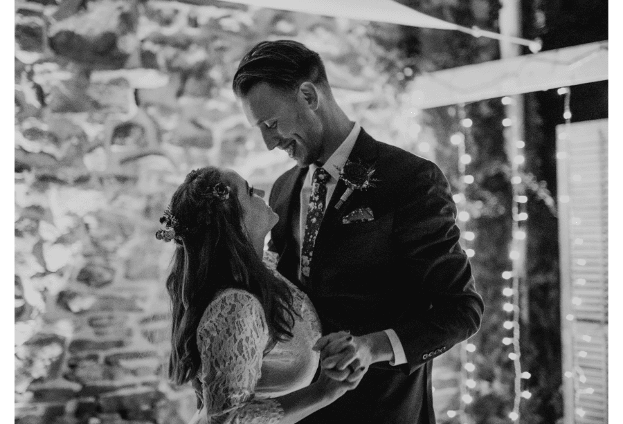 A couple shares a romantic moment during their wedding against a softly lit stone wall.