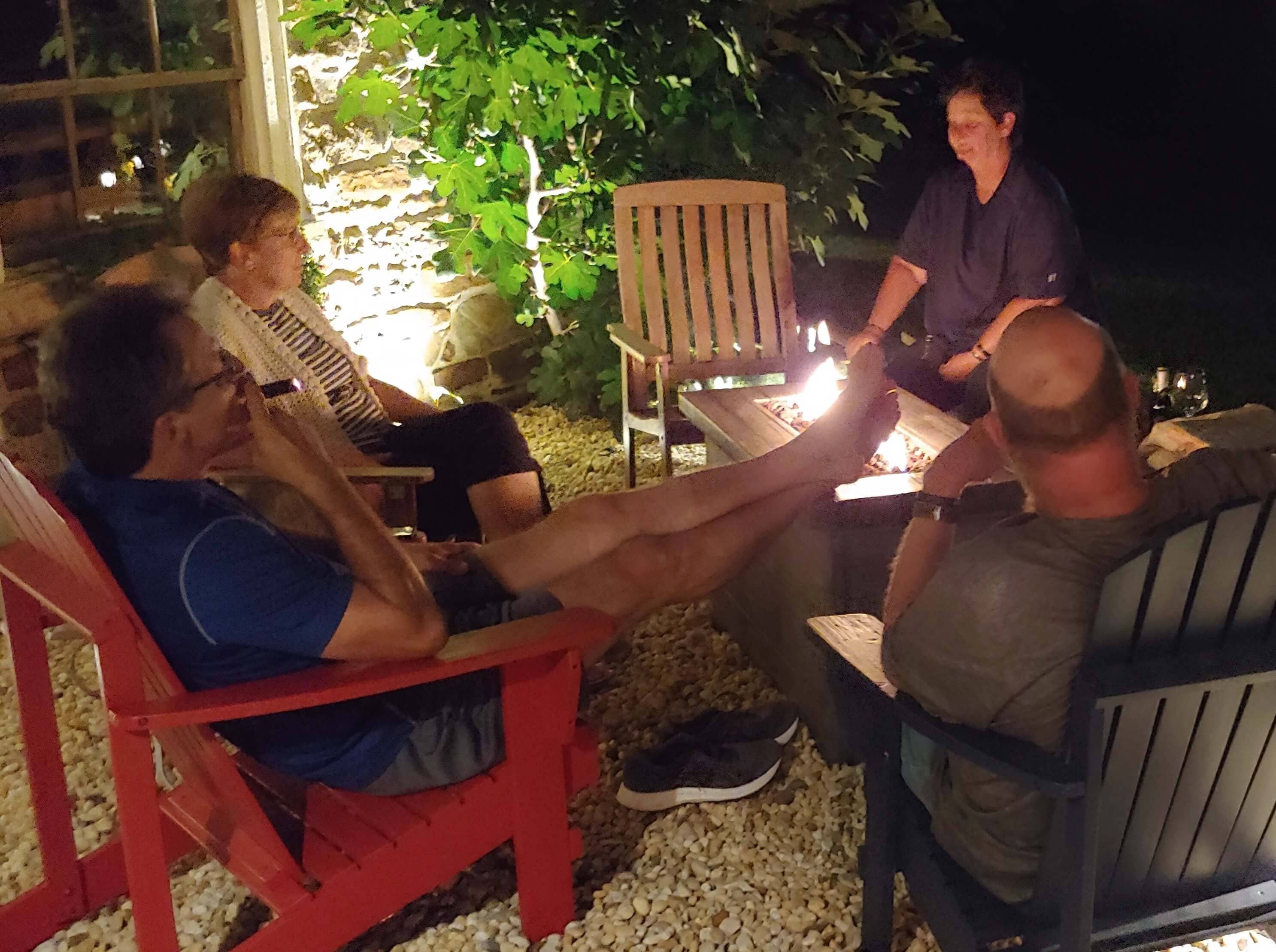 A group of four people sitting around a fire pit at night, enjoying each other's company.