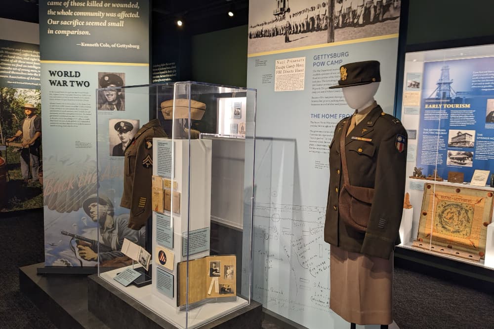A military exhibit showcasing World War II memorabilia, including uniforms and photographs, in a museum setting.