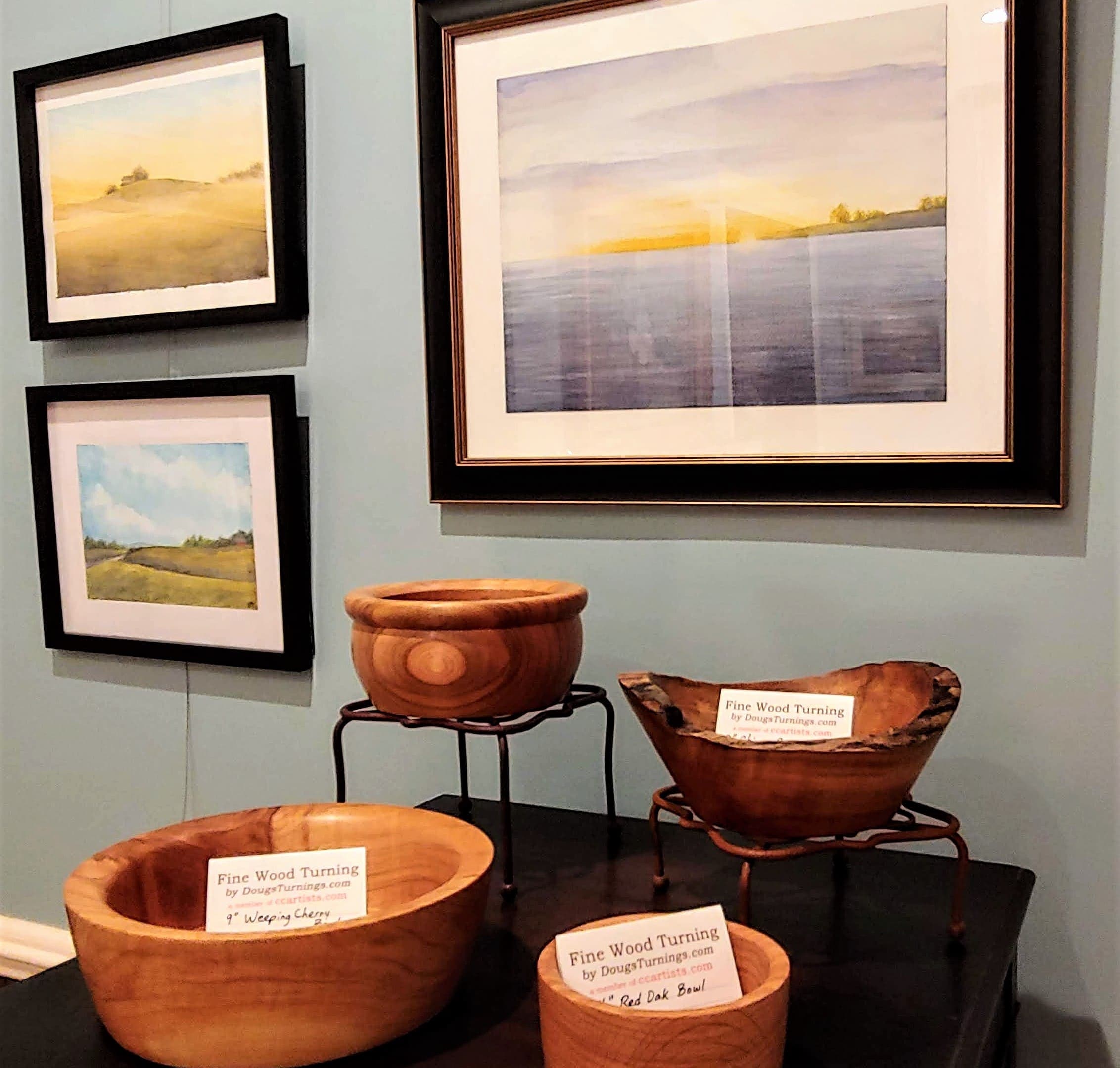 A display featuring wooden bowls and framed landscape paintings on a wall.