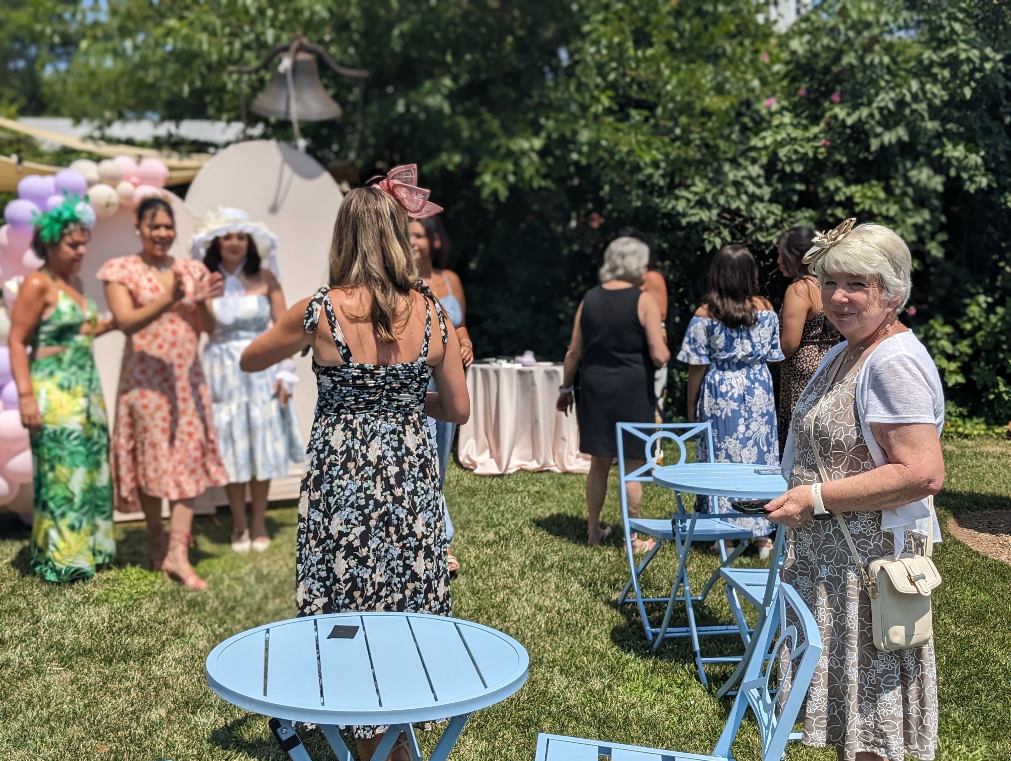 A group of women dressed in colorful dresses gather in a garden setting with tables and decorations.