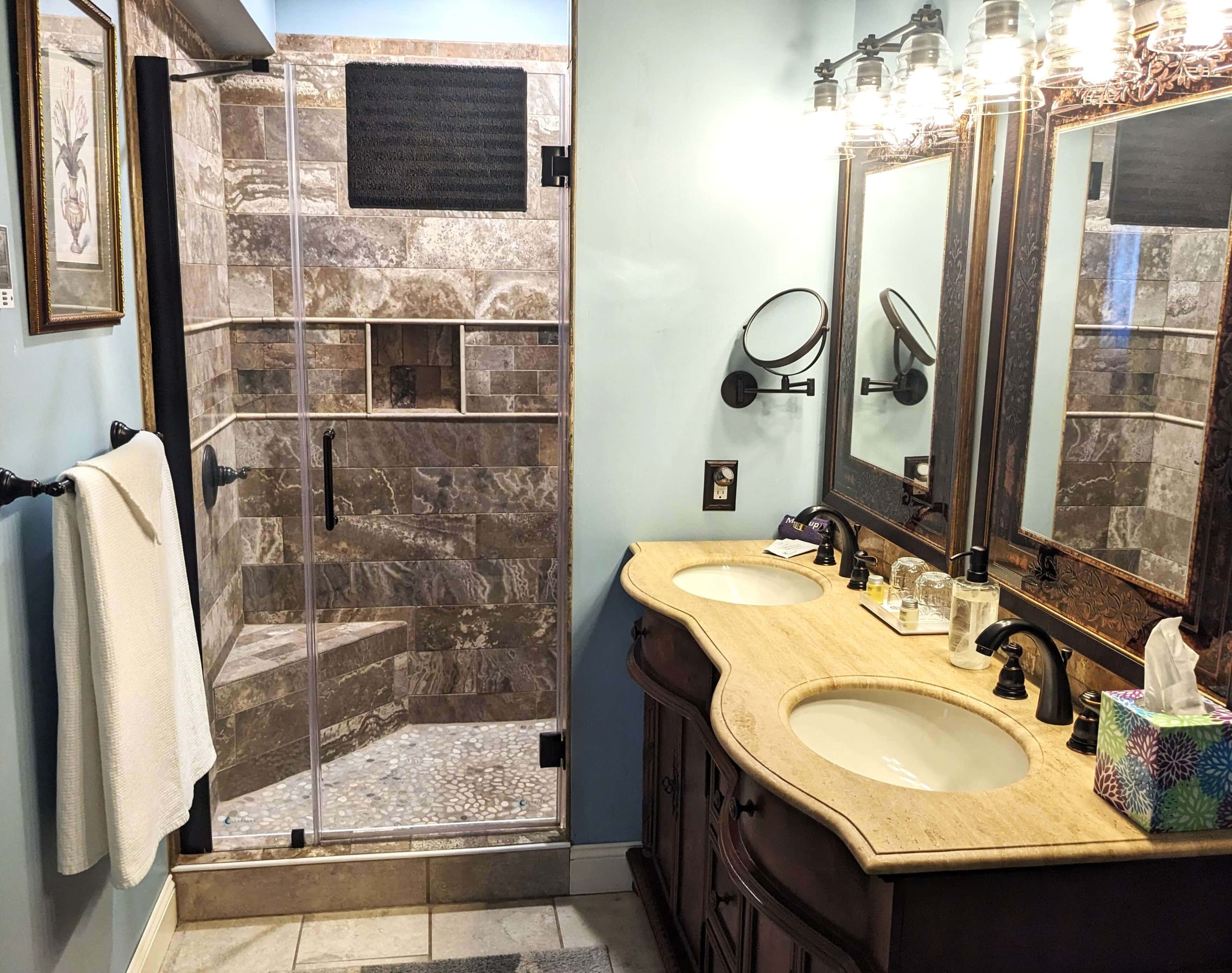 A modern bathroom featuring dual sinks, a glass shower, and decorative lighting.