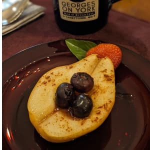 a baked pear topped with fresh blueberries, and a strawberry half, in front of a Georges on York coffee mug